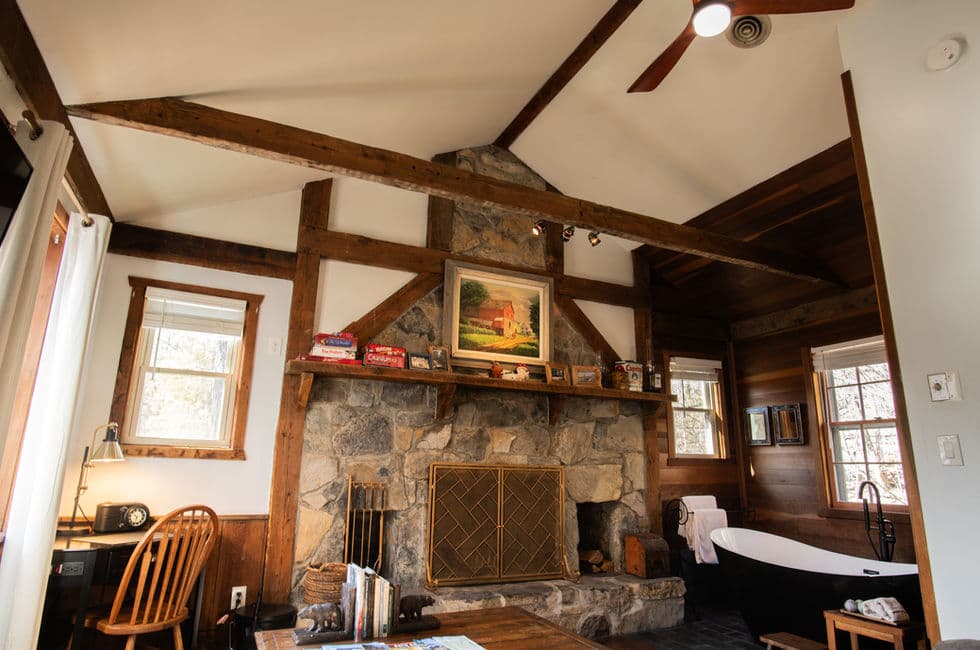 Rustic cabin interior with large stone fireplace, exposed beams, and black & white slipper tub.
