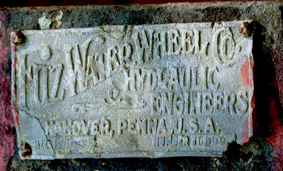 A weathered metal plate identifying "Fitz Water Wheel Co. Hydraulic Engineers" from Hanover, Pennsylvania, USA.