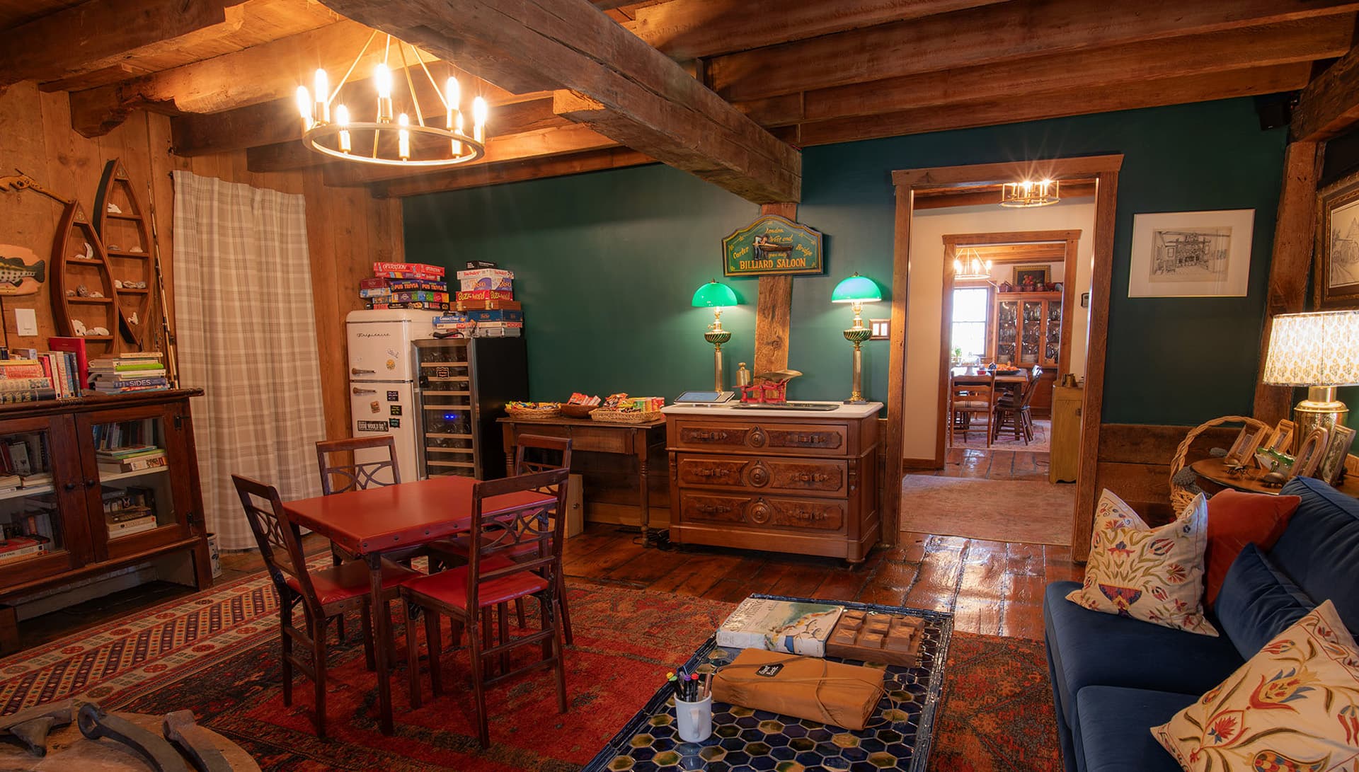 A cozy room featuring wooden beams, a red dining table, vintage decor, and shelves filled with board games and books.