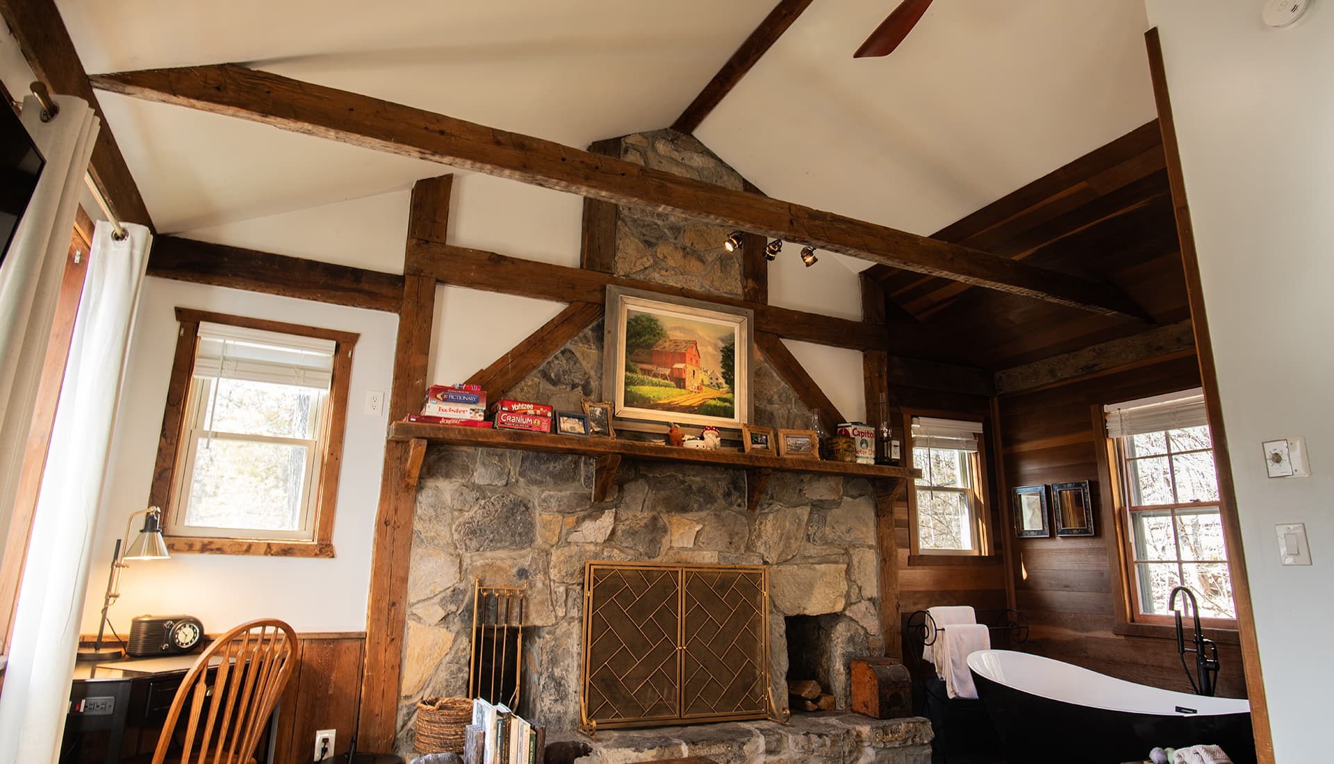 Cozy living space featuring a stone fireplace, wooden beams, and a freestanding bathtub.